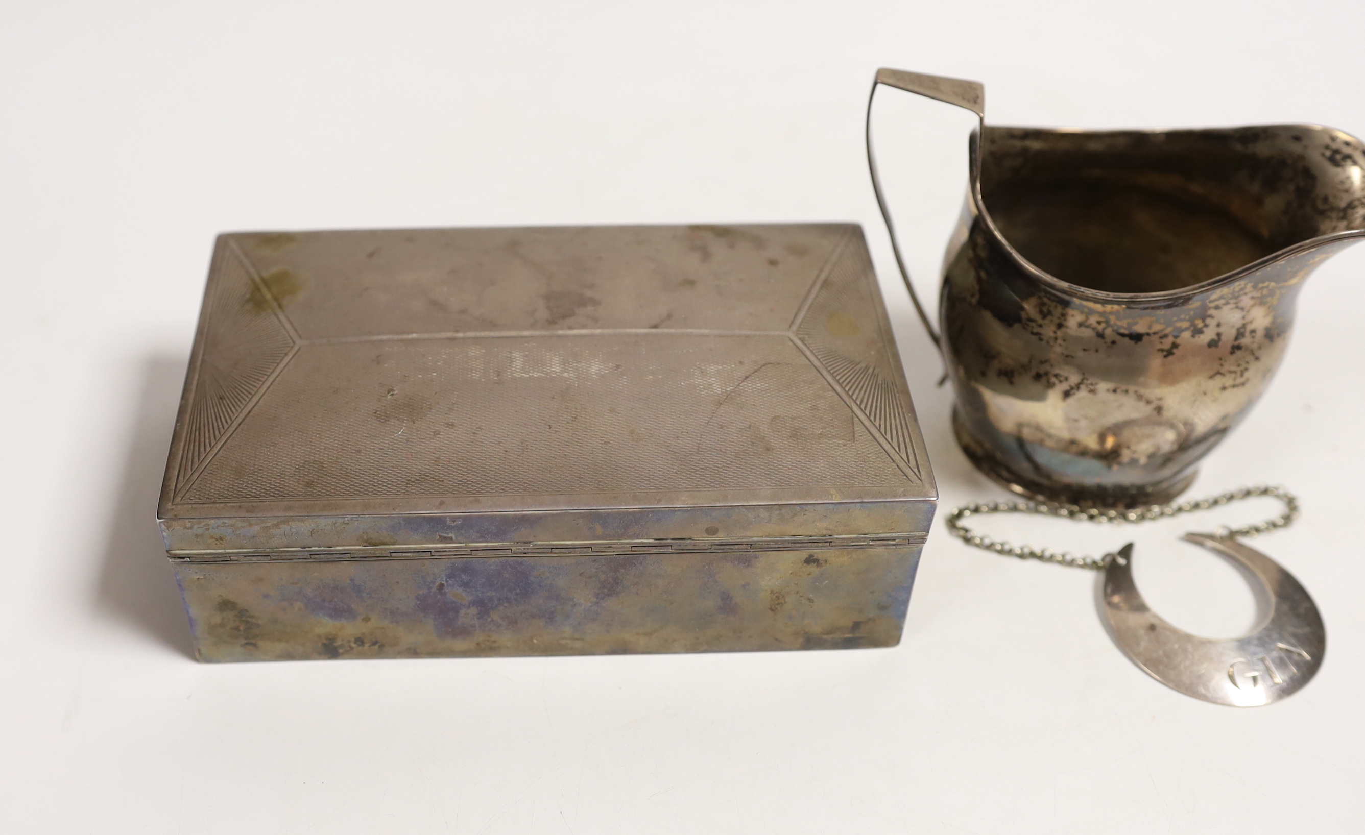 A George V Art Deco silver mounted rectangular cigarette box, with engraved inscription, Birmingham, 1932, 15.1cm, a Georgian silver cream jug, maker possibly William Welch II of Exeter? and a Georgian silver crescent 'G